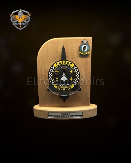 Wooden Commemorative Desk Plaque This wooden display plaque is built for official military and corporate presentations. The item features a solid light wood backboard mounted on a stable wooden base. It includes custom metal emblems and an engraving plate for specific event details. A matching presentation box accompanies the plaque for formal gifting. Product Specifications Build: Solid wood base and main board integrated with custom metal attachments. Detailing: Large central 3D metal crest and a secondary badge on the top right corner. Text Plate: Dedicated metal plate at the base for personalized text, names, and dates. Packaging: Secure presentation box featuring a custom logo on the lid to match the plaque design. Custom Production Details Wooden plaques with integrated metal badges are standard requirements for unit milestones, retirements, and corporate awards. The combination of custom wood shaping, detailed metal casting, and branded packaging highlights the manufacturing capacity available for specialized institutional orders. We produce these commemorative items according to exact unit and corporate specifications.